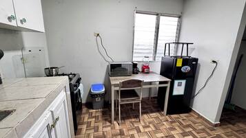 Une cuisine de taille réduite équipée d’une cuisinière à gaz, d’un four à micro-ondes, d’un réfrigérateur et d’une fenêtre avec des stores.