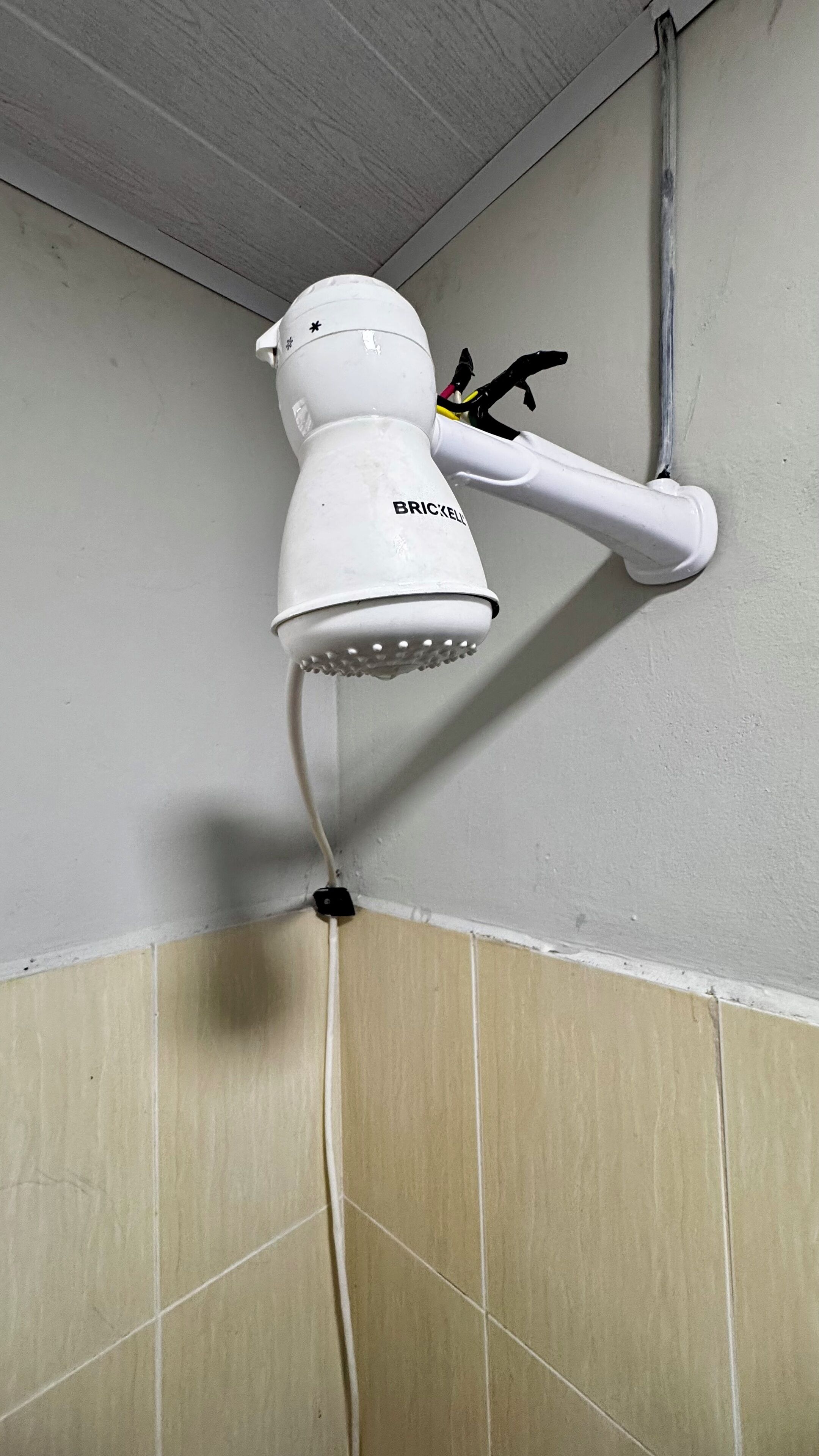 A white wall-mounted showerhead with a flexible hose, attached to a wall with a corner tile design.