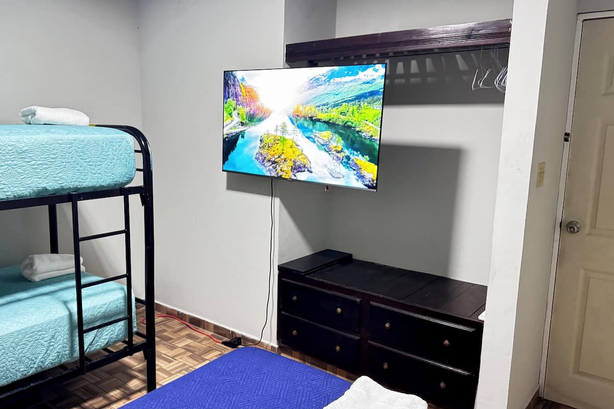 A room with bunk beds, a flat-screen TV mounted on the wall, a dresser, and a door.