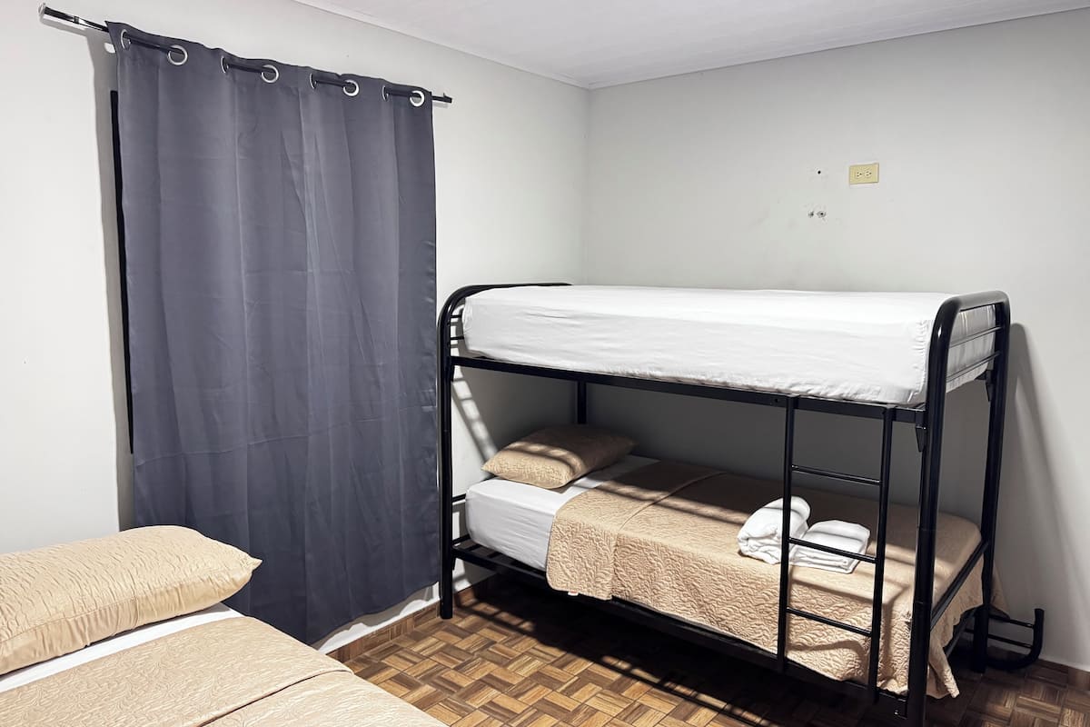 A bunk bed room with a curtain, a wooden floor, and a small electrical outlet on the wall.