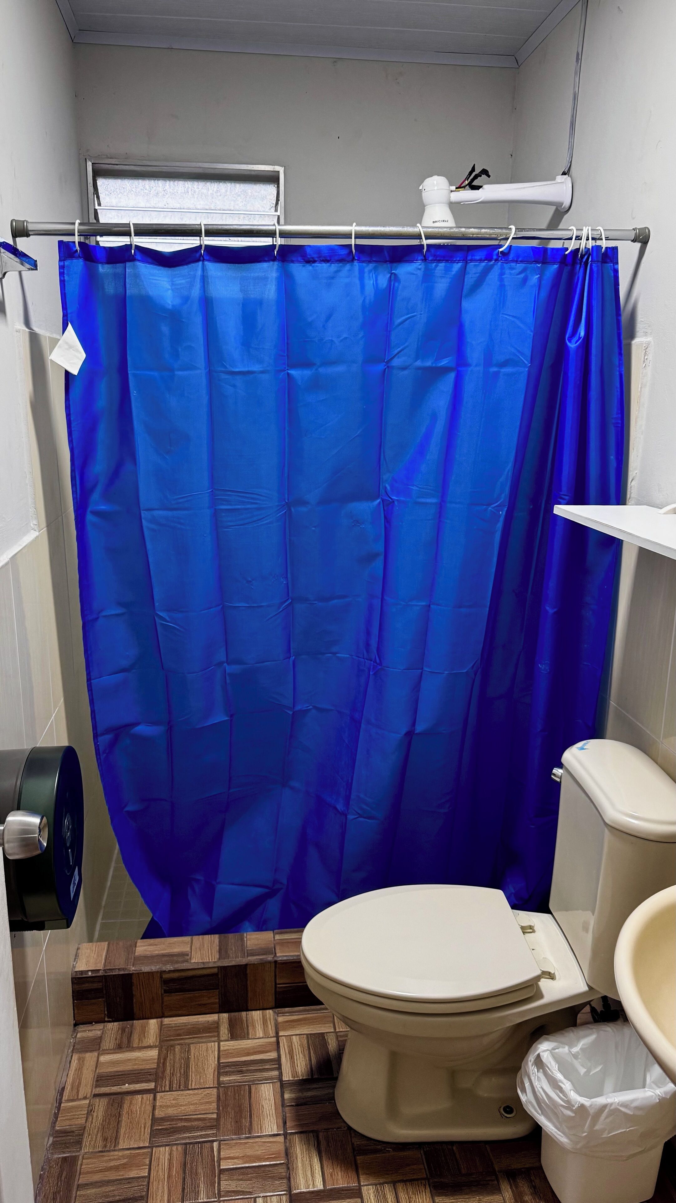 A small bathroom with a toilet, a shower curtain, and a waste bin.