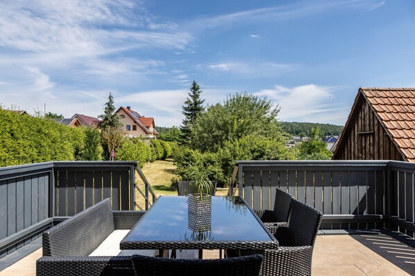 An outdoor patio with a table and chairs, surrounded by a wooden fence and greenery.