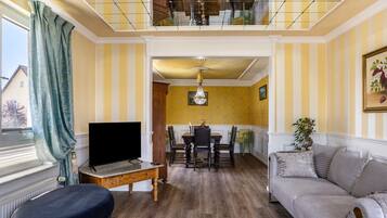 A living room with a TV, sofa, dining table, and chairs.