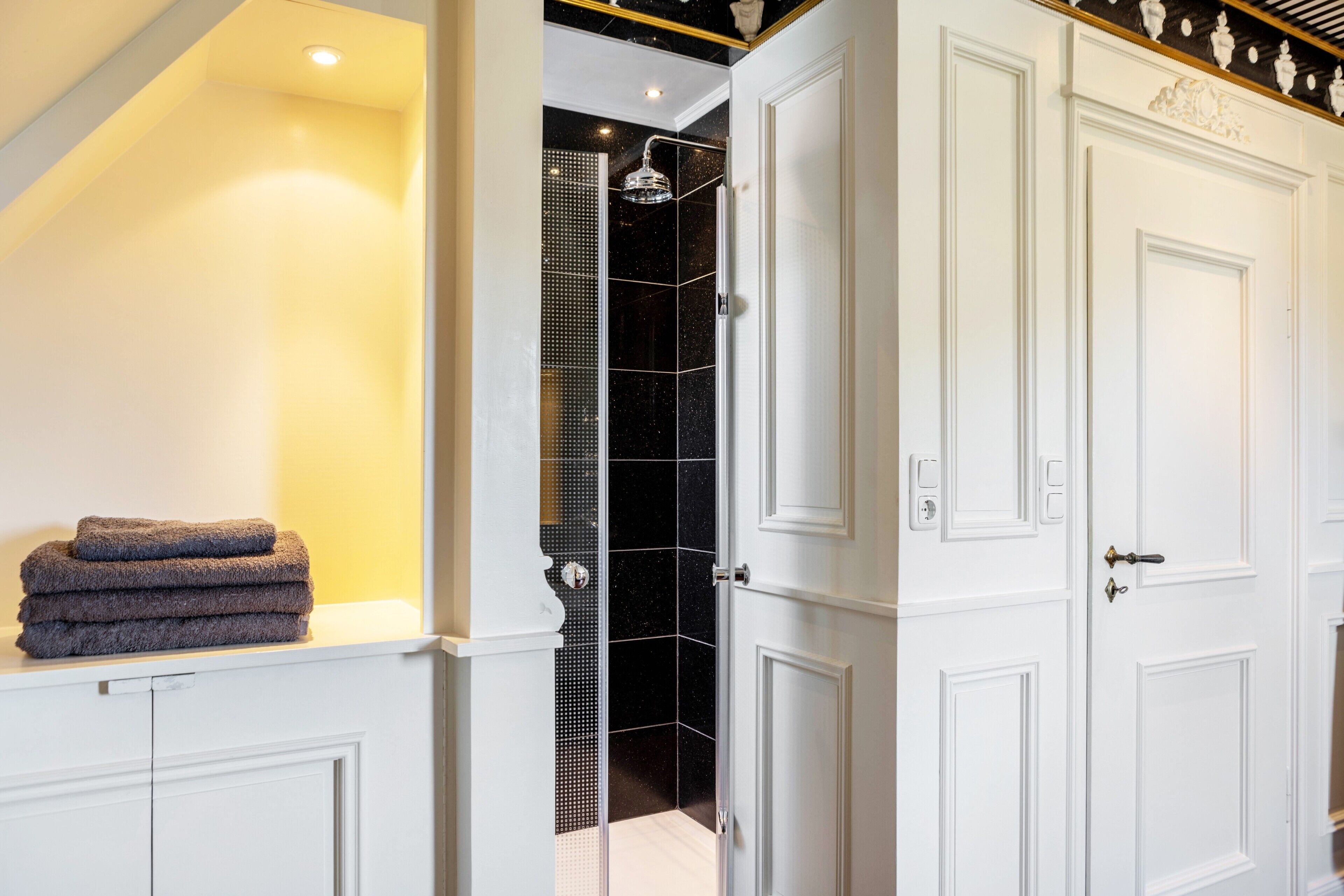 A bathroom with a shower, a stack of towels, and a white door.