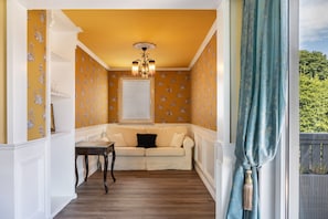A room with a yellow wall, a white ceiling, a wooden floor, a white sofa, a small table, and a window with a curtain. - Holiday Home 'Ferienhaus Barockhaus Fulda' with Private Terrace, Private Garden and Wi-Fi (Petersberg)