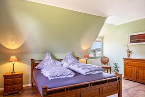 A bedroom with a bed, nightstand, lamp, chair, and a view of the outside.