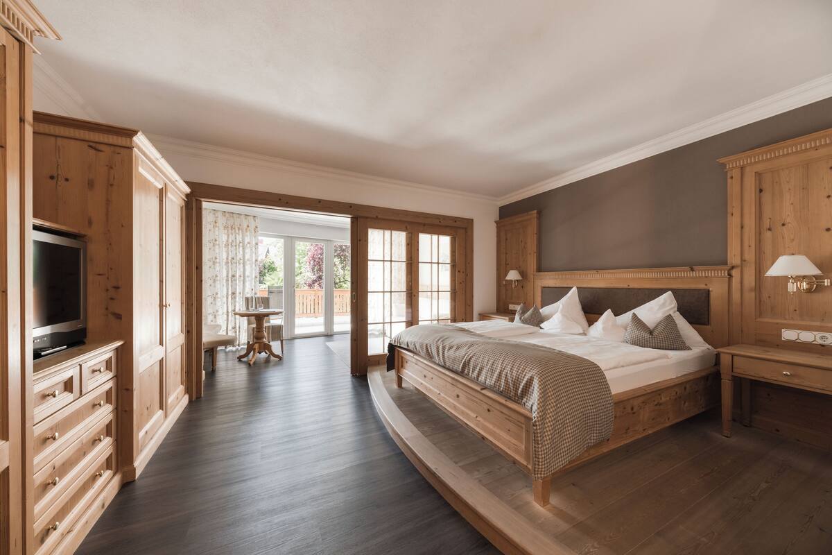 Une chambre avec un grand lit, des meubles en bois, une télévision et une vue sur l’extérieur.