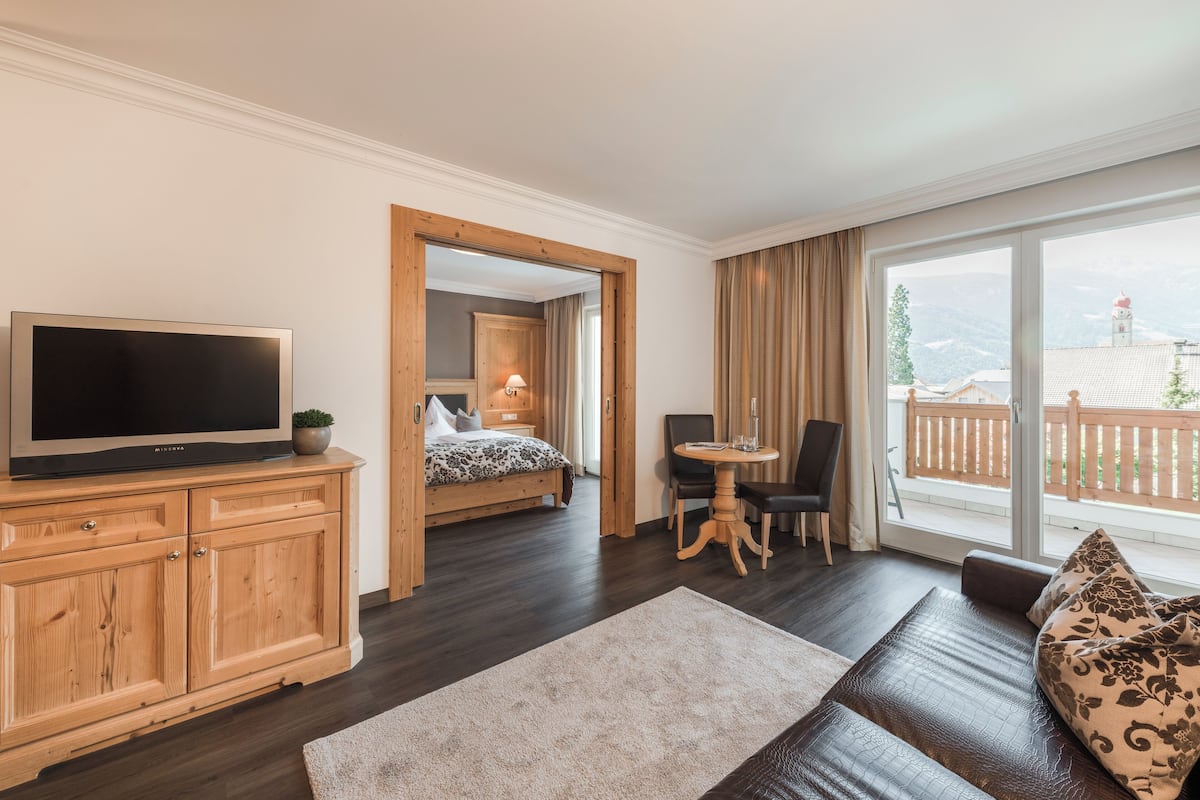 Une chambre d’hôtel moderne dotée d’une grande télévision, de meubles en bois, d’un lit confortable, d’un coin repas et d’un balcon offrant une vue sur les montagnes.