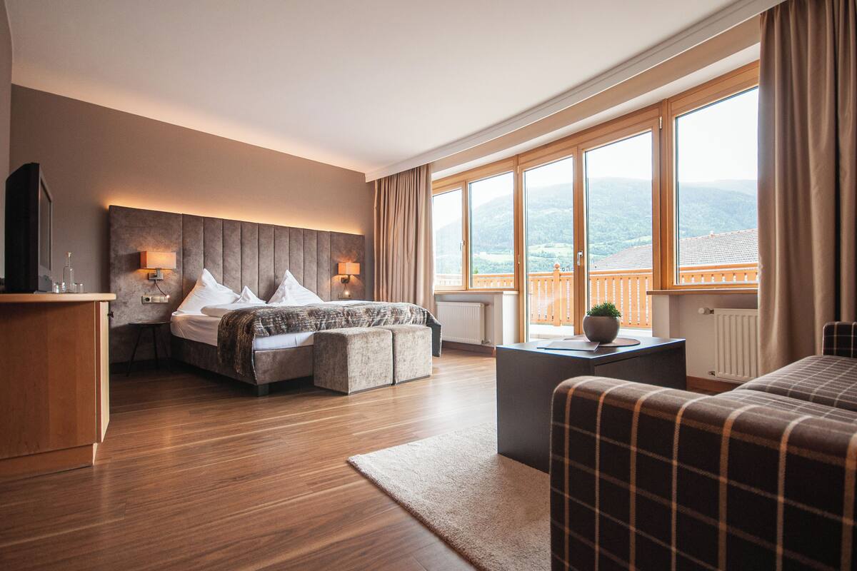 Une chambre d’hôtel moderne dotée d’un grand lit, d’un coin salon et d’un balcon offrant une vue sur la montagne.