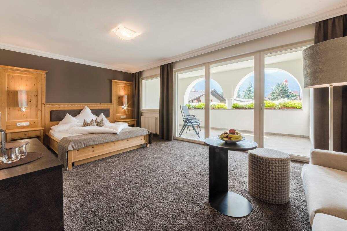Une chambre d’hôtel moderne avec un grand lit, une petite table ronde et une vue sur l’extérieur grâce à de grandes fenêtres.