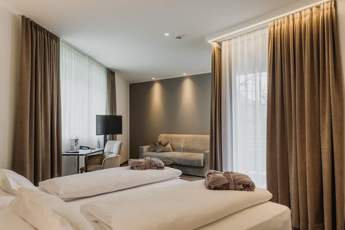 Une chambre d’hôtel avec deux lits, un bureau avec une chaise, un canapé et une télévision.