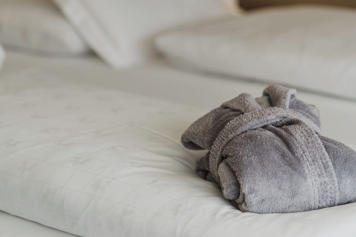 Un lit bien fait, avec du linge de lit blanc et une serviette grise pliée posée sur le bord.