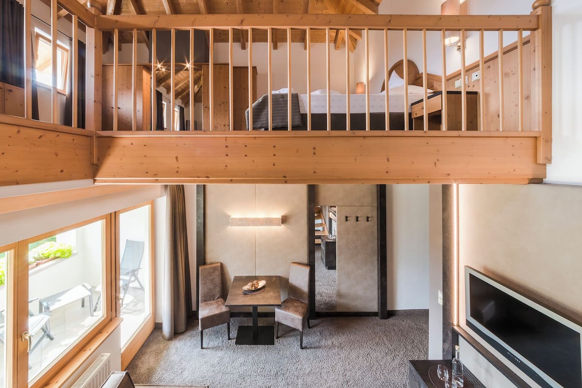 Une chambre de style « loft » avec un balcon en bois, un coin repas avec une table et des chaises, et un téléviseur fixé au mur.