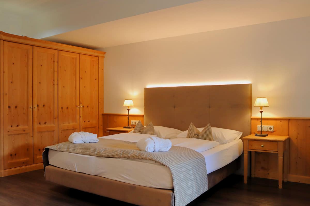 Une chambre d’hôtel avec un grand lit, une armoire en bois, deux tables de chevet avec des lampes et une tête de lit dotée d’un éclairage intégré.