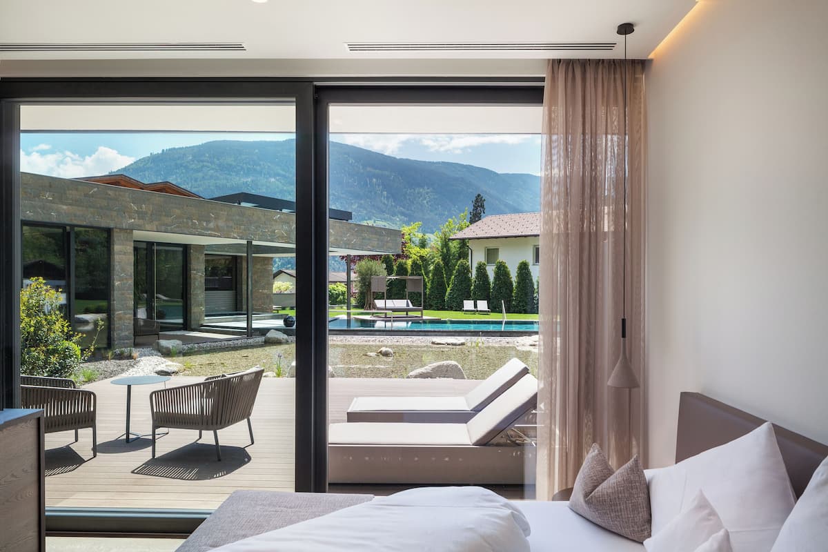 Une chambre d’hôtel moderne dotée d’une grande porte-fenêtre coulissante donnant sur une terrasse avec une piscine et des chaises longues.
