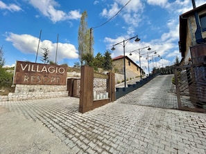 Een bord met 'VILLAGIO RESORT', een stenen muur en een verhard pad dat naar een gebouw leidt.