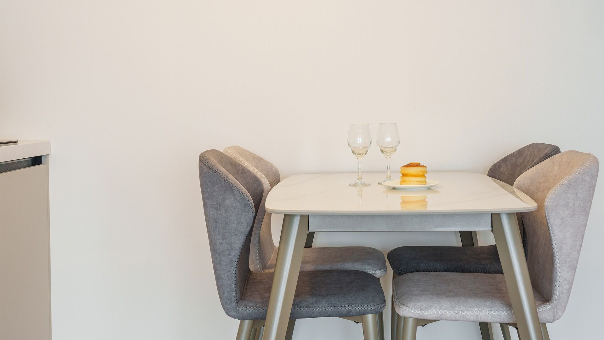 A small dining table with two chairs, two wine glasses, and a dessert on a plate.