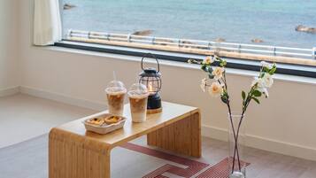 A wooden table with drinks and pastries, a lantern, and a vase with flowers by a window overlooking water.