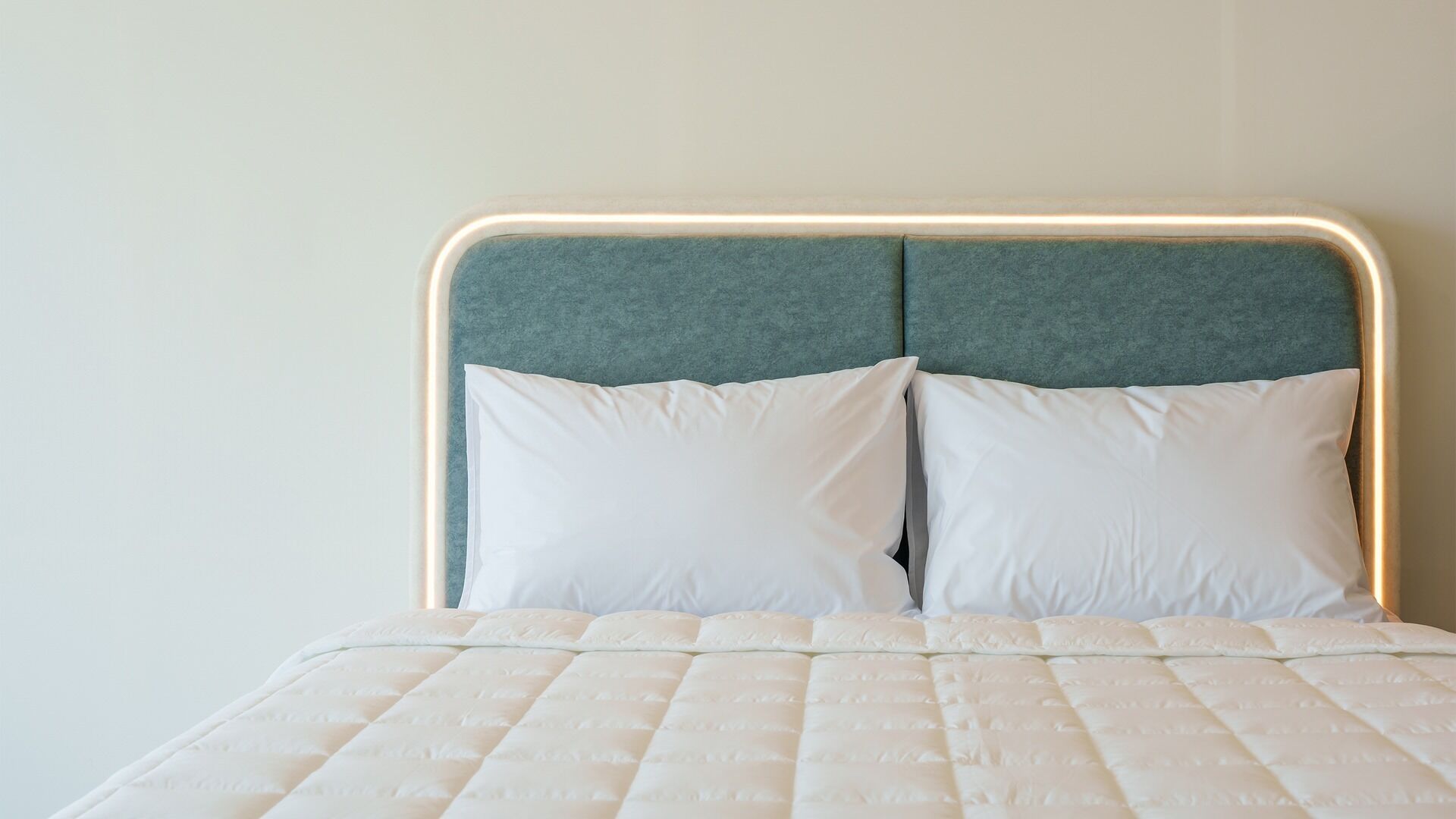 Una cama con colchón acolchado y dos almohadas, cabecera con tira de luz y pared lisa.