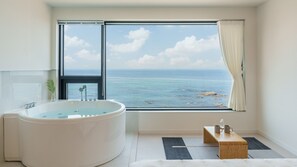 Een moderne badkamer met een ruime badkuip, een houten bankje en uitzicht op zee.