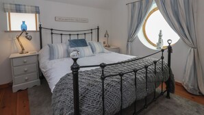 Un dormitorio con una cama con dosel, una lámpara de noche, una mesita de noche, una ventana con cortinas y un adorno en la pared.