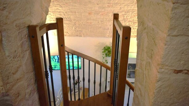A wooden staircase with a white wall and a view of a green outdoor area. - Arcaica cummersa - Dimora in pietra (Alberobello)