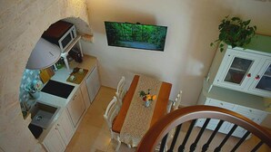A kitchen with a microwave, sink, and dining table with chairs. There is a framed picture on the wall and a plant on the right. - Arcaica cummersa - Dimora in pietra (Alberobello)