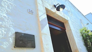 A building with a white exterior, a numbered plaque, and a metal sign with text. - Arcaica cummersa - Dimora in pietra (Alberobello)
