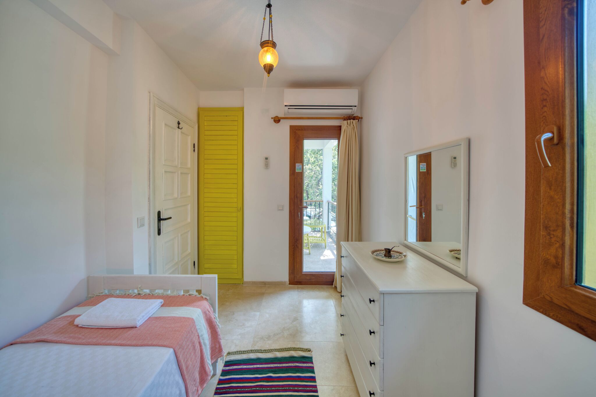 A bedroom with a bed, a dresser, a mirror, and a door leading to a balcony.