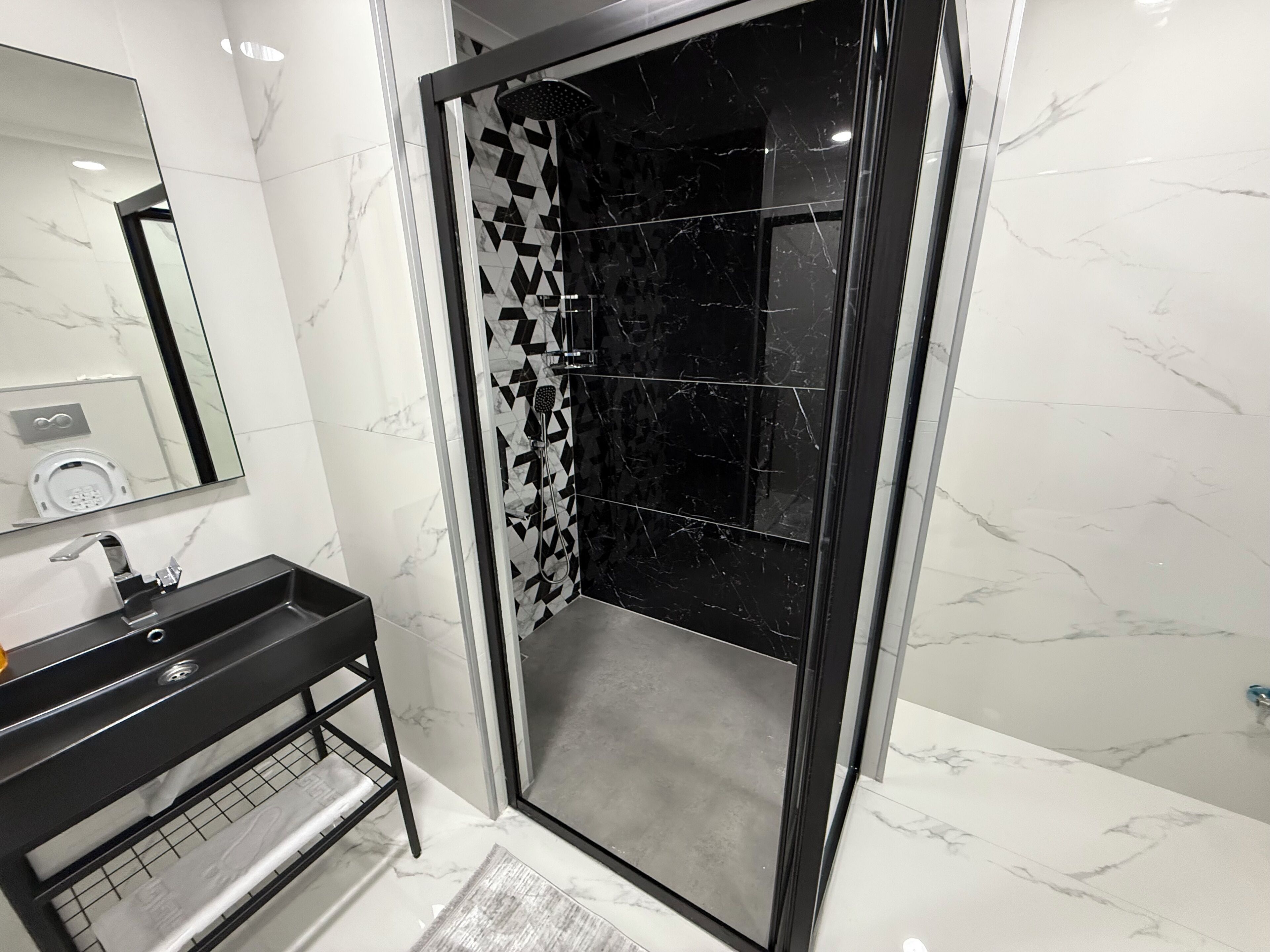 A modern bathroom with a black shower enclosure, a black sink, and a mirror.