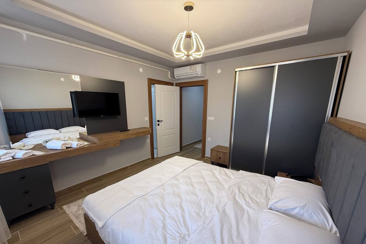 Un dormitorio con cama, televisión, escritorio con silla, armario y puerta.