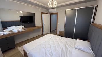 A bedroom with a bed, a TV, a desk with a chair, a wardrobe, and a door.