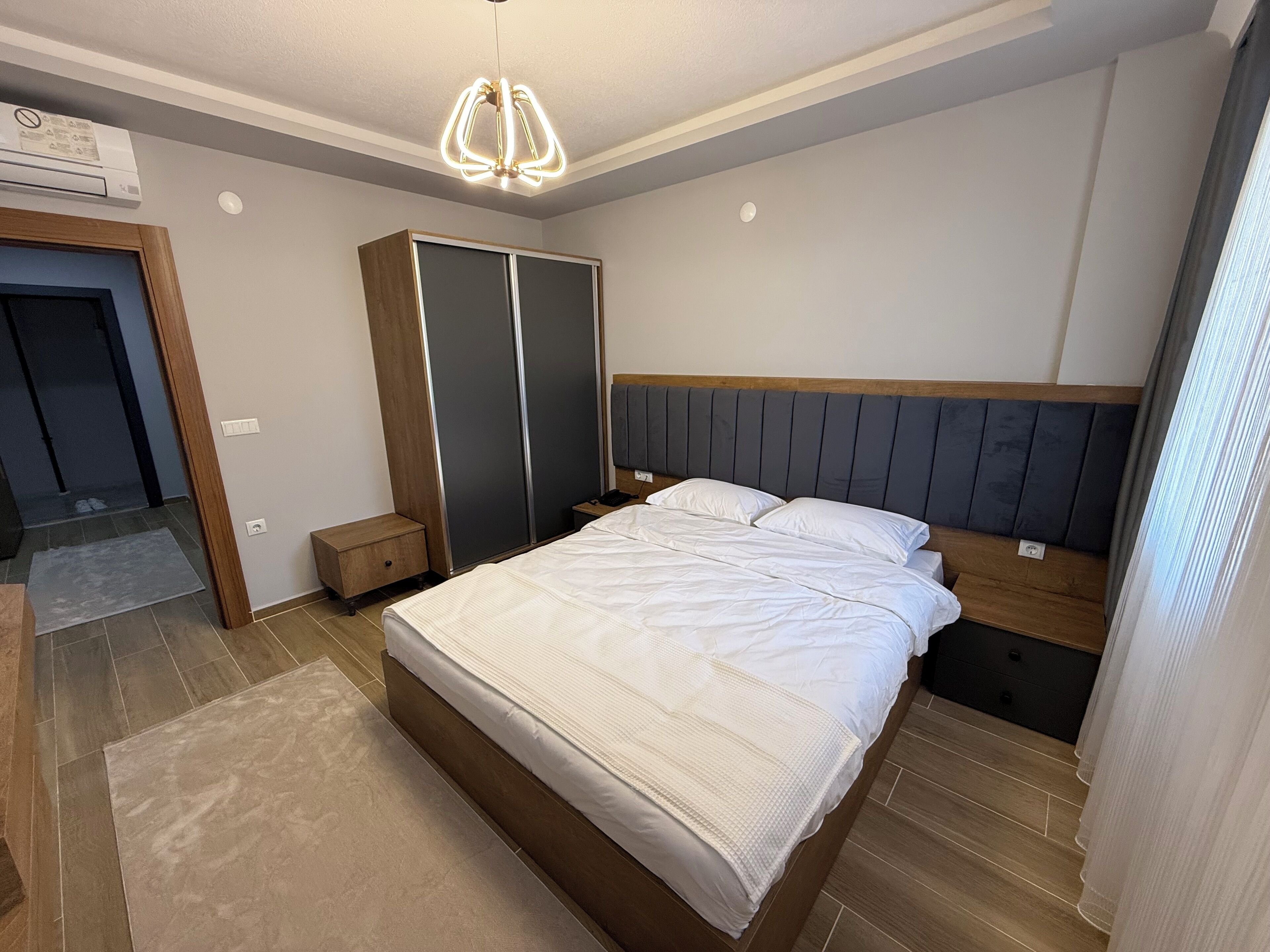 A bedroom with a bed, bedside tables, a wardrobe, and a modern light fixture.