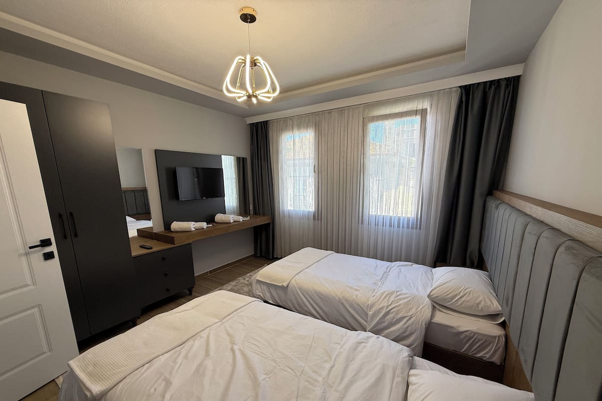Habitación de hotel con dos camas, televisor, escritorio y un ventanal grande con cortinas.