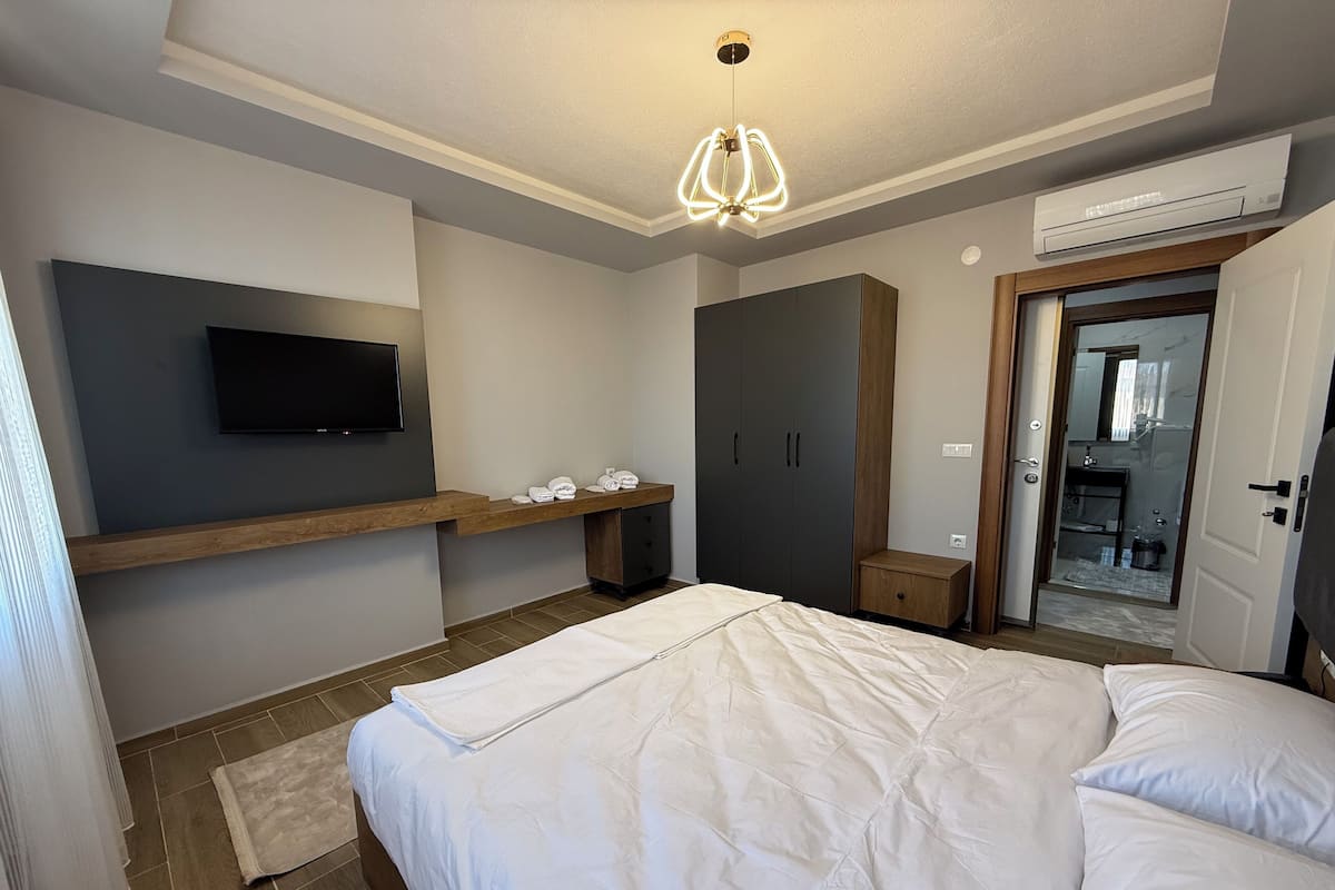 Un dormitorio moderno con una cama, un televisor montado en la pared, un armario y un equipo de aire acondicionado.