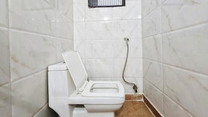 Een kleine, witte badkamer met toilet, douche en een raam met tralies.