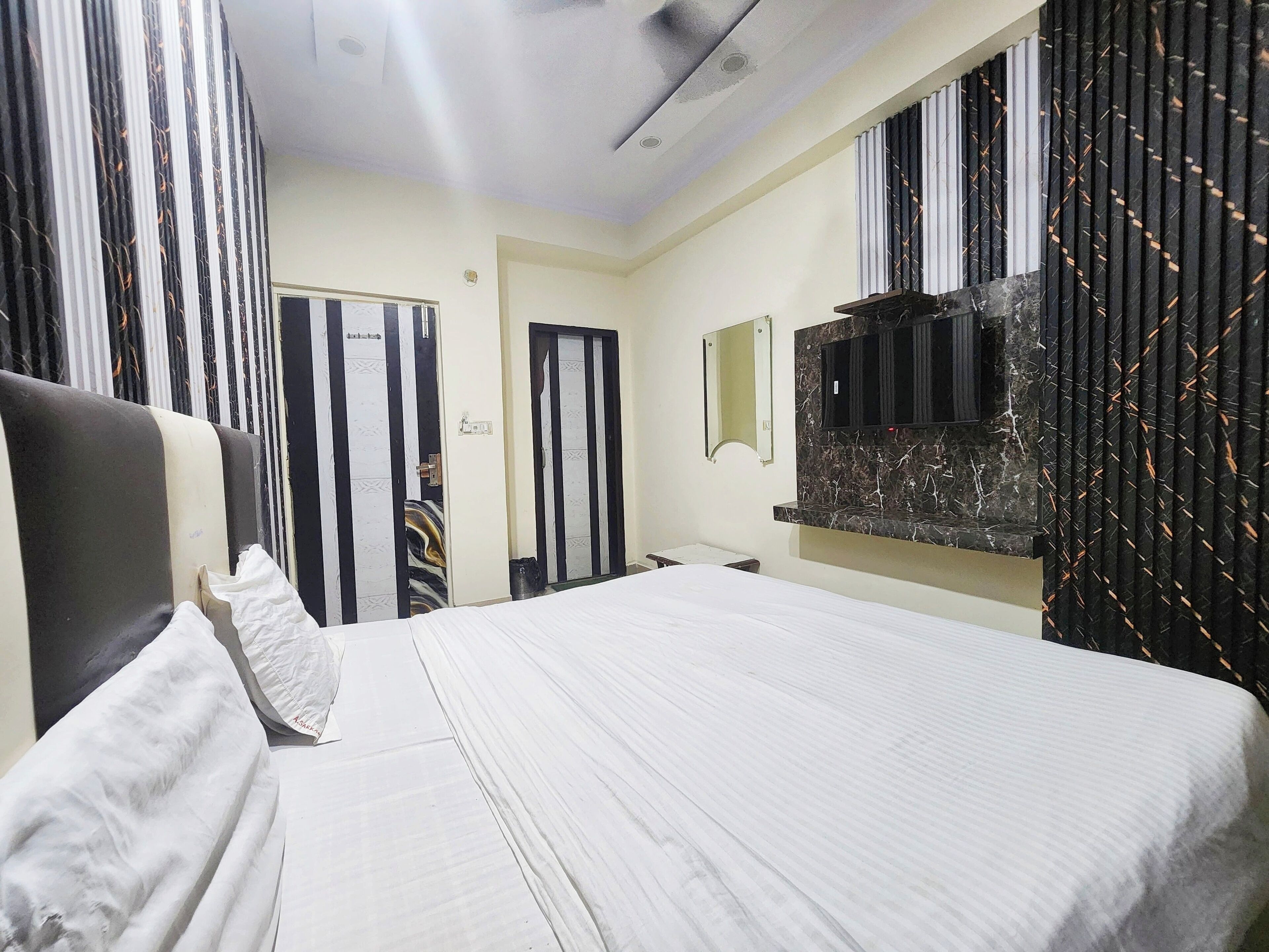 A hotel room with a bed, a TV mounted on the wall, a mirror, and striped curtains.