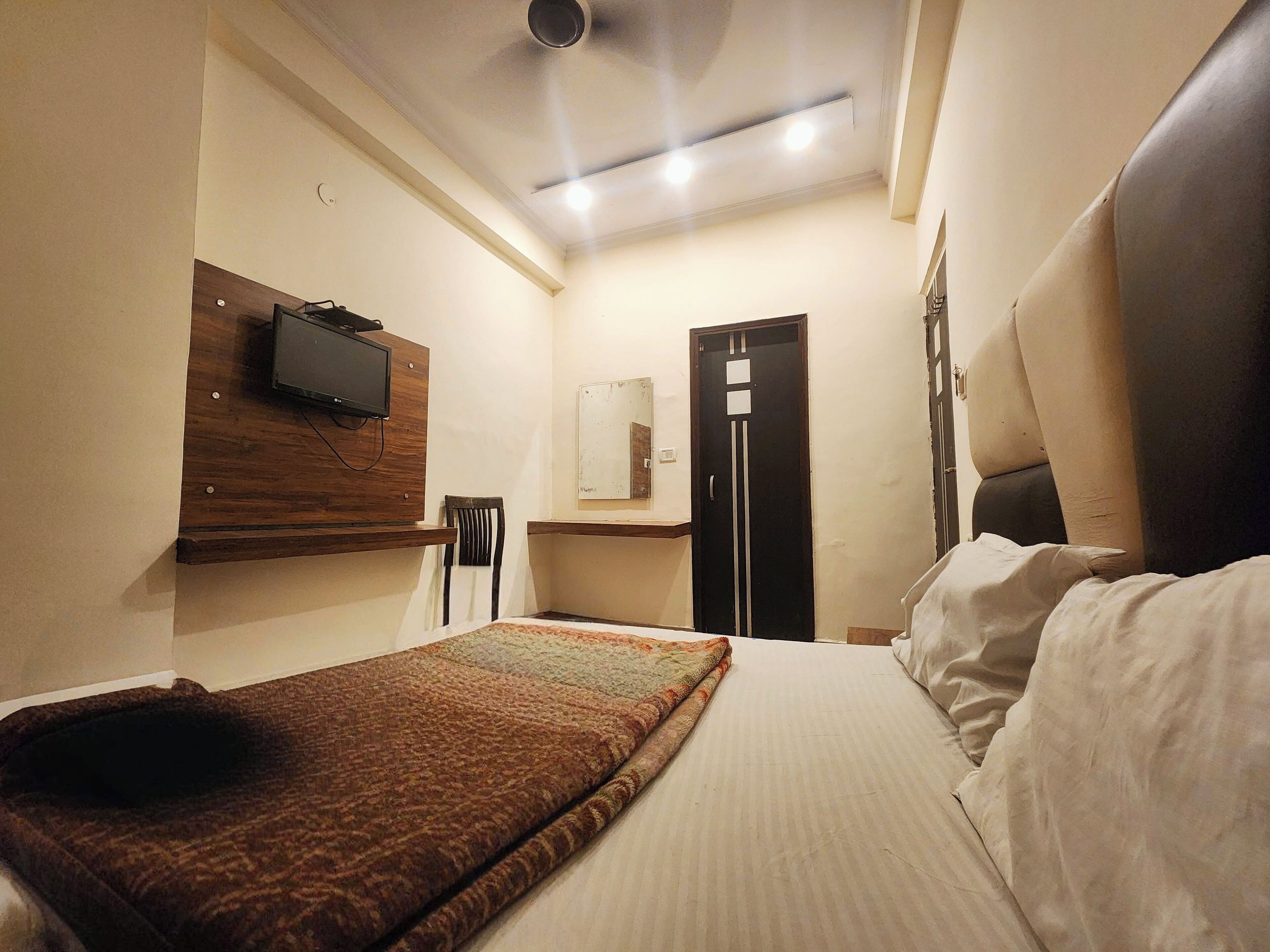 Habitació d'hotel amb un llit, una televisió penjada en un panell de fusta, un escriptori amb una cadira i una porta.