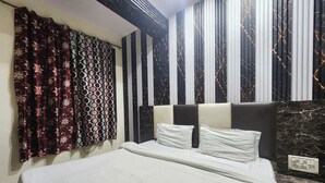 Een bed met een wit sprei en twee kussens, een hoofdbord met een zwart-wit patroon en gordijnen met een bloemenprint.