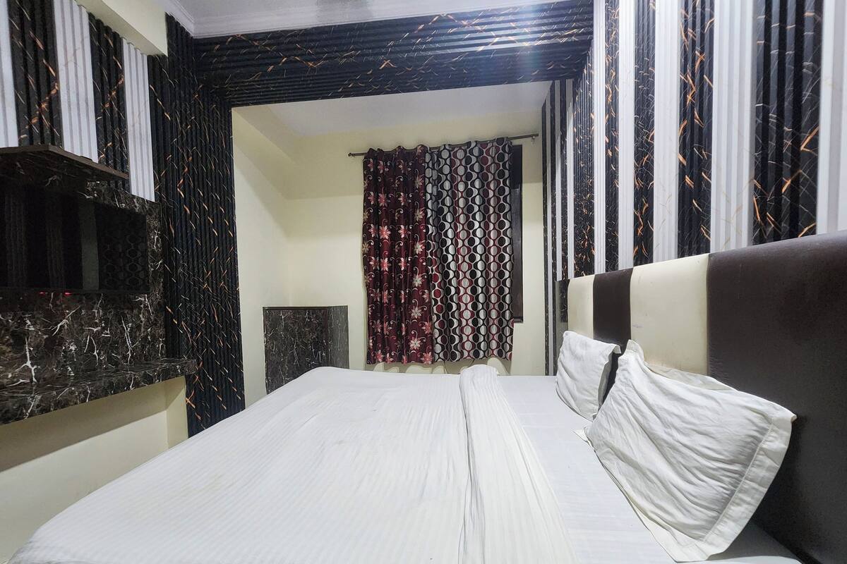 A neatly made bed with white linens and pillows, a dark headboard, and a patterned curtain in the background.