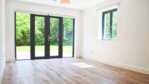 Una habitación con piso de madera, puerta corrediza de vidrio que da a un jardín y una ventana pequeña.