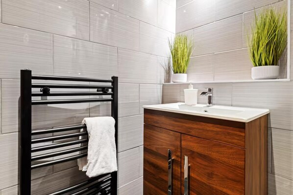 Un baño moderno con toallero negro, lavamanos blanco y muebles de madera.