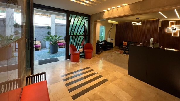 Un espace d’accueil moderne comprenant un comptoir de réception, un coin salon et une porte vitrée donnant sur un espace extérieur agrémenté de plantes.