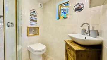A bathroom with a toilet, a sink, and a shower. There are decorative items on the wall, including a framed picture and a sign with various phrases.