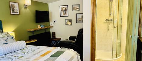 A bedroom with a bed, a desk, a chair, a TV, and a shower room.