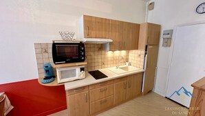 Cocina compacta con armarios de madera, microondas, cafetera y refrigerador.