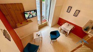 Un espacio habitable compacto con una televisión, una mesa de comedor, dos sillas, una mesita con un control remoto y una ventana con vistas a la calle.