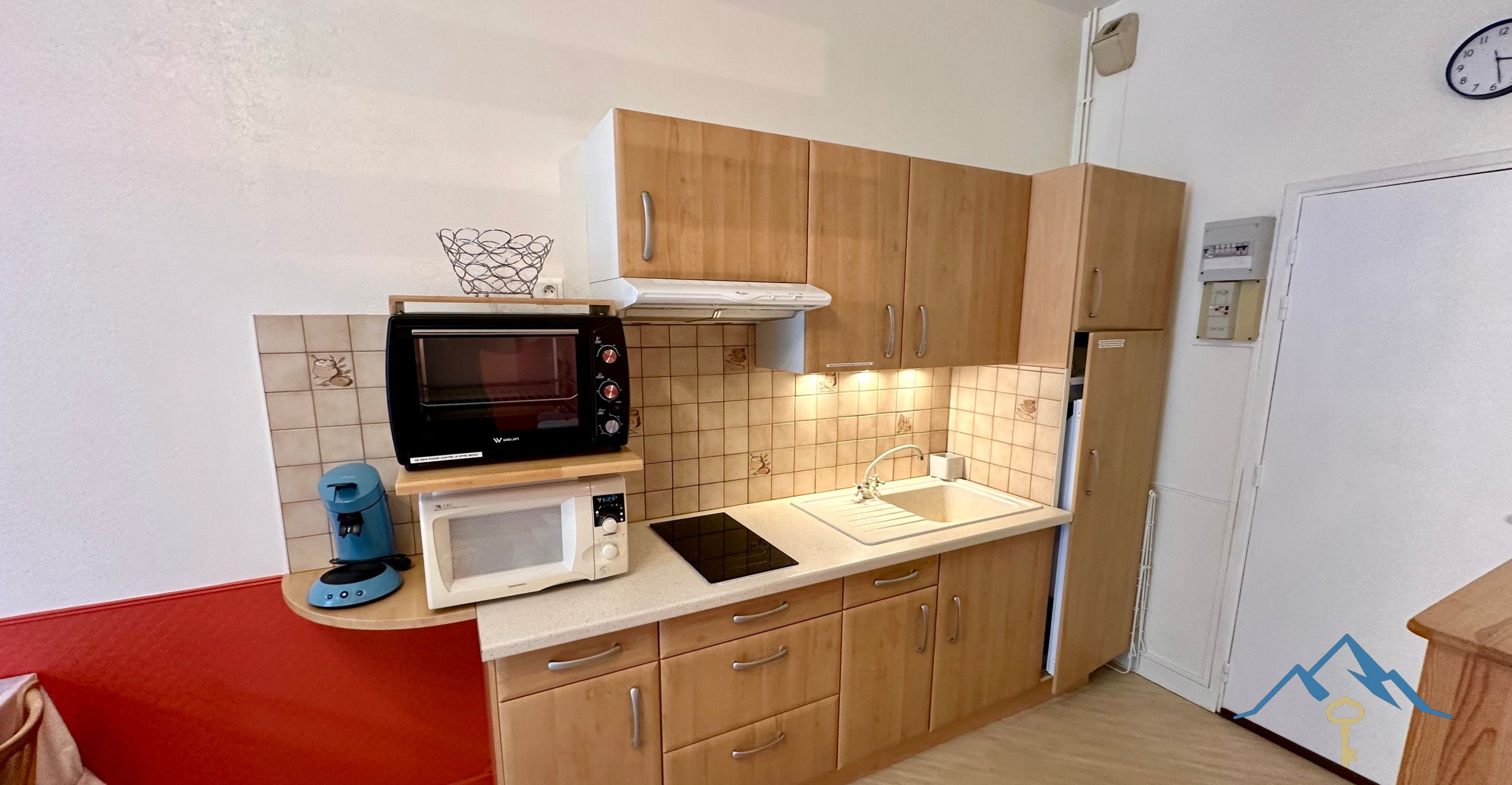 A compact kitchen with wooden cabinets, a microwave, a coffee maker, and a refrigerator.