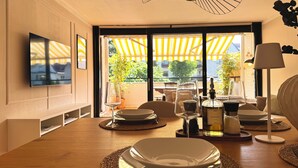 Een eethoek met een houten tafel voor twee personen, een aan de muur bevestigde televisie en uitzicht op het landschap door grote ramen.