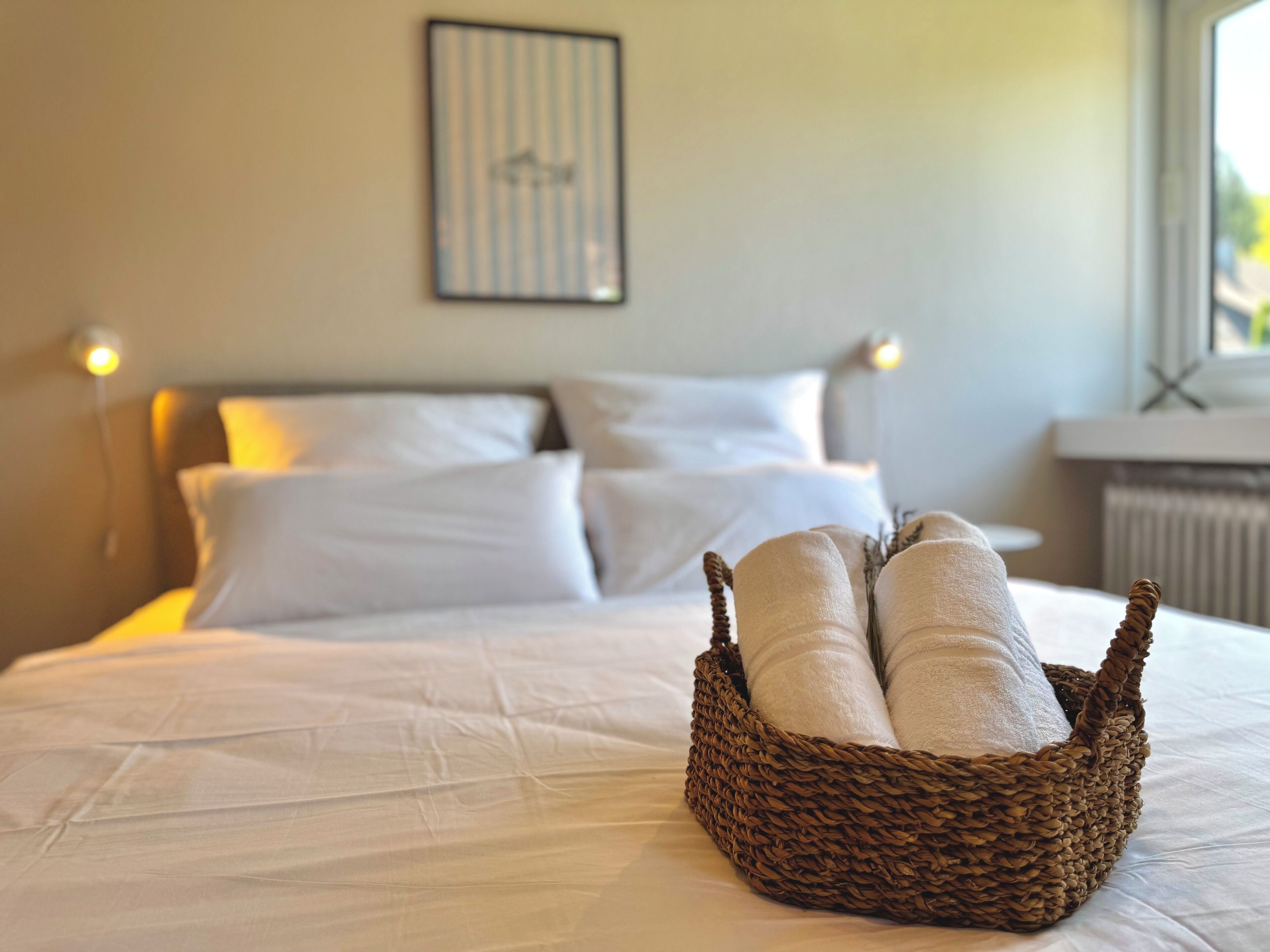 Un lit bien fait, avec du linge de lit blanc et un panier en osier contenant des serviettes pliées, posé sur le lit.